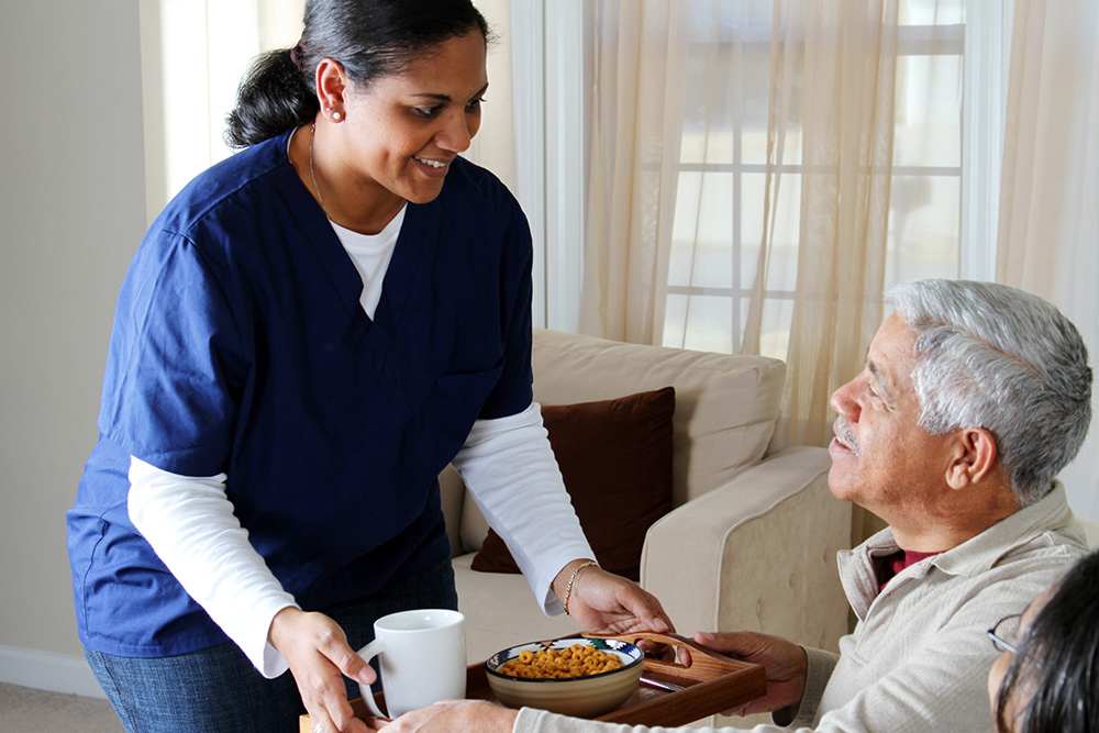 A young, smiling woman serving a meal to an older person